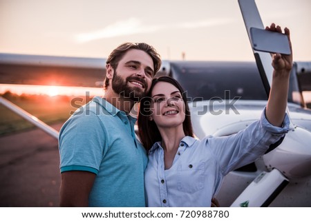 Beautiful romantic couple is using a smart phone and smiling while doing selfie on take-off ground near the aircraft