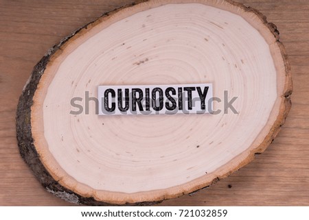 The word "Curiosity" written on a white strip and placed on top of a tree stump. With wooden backdrop.