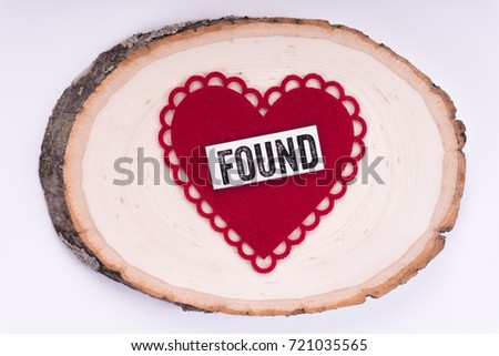 The word "Found" written on a white strip and attached to a heart. Placed on top of a tree stump. Isolated in white backdrop.