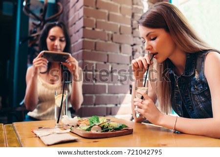 Two girlfriends having healthy lunch in cafe. Young woman taking picture of food with smartphone posting on social media