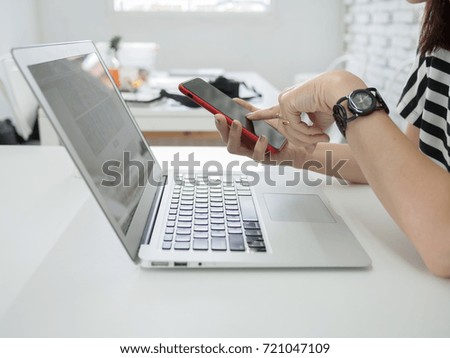 Asian woman holding smart phone with laptop computer while sitting in coffee shop