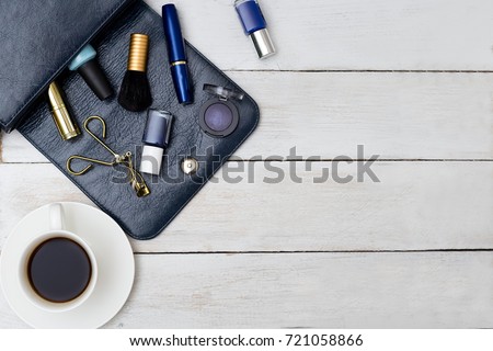 Female handbag of dark blue color and cosmetics with cup of coffee