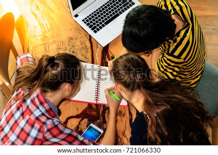 Education Concept: A young handsome boy and young beautiful girls is working together for doing their report or they are reading some textbook to prepare for some test tomorrow with top view photo.