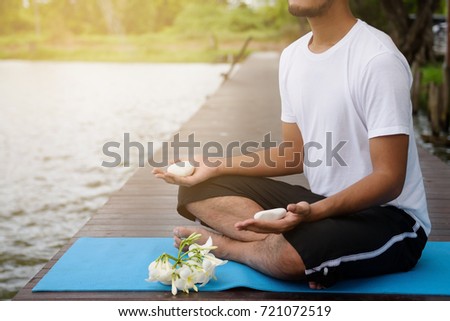 Yoga Male meditation exercise with white rock on hands on wooden bridge at lakes against sunlight. Healthcare and Fitness concept with copy space for text.