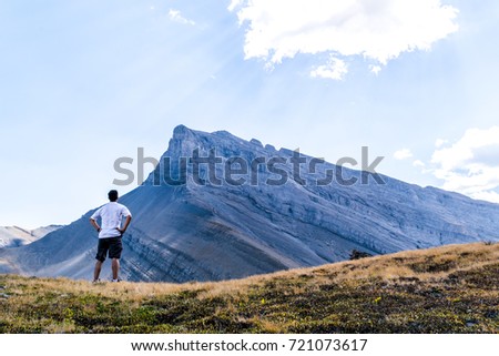 Male hiker with white shirt looking up at a mountain peak Royalty-Free Stock Photo #721073617