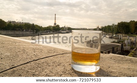 a glass of whiskey at the foot of the Seine river, with the eiffel tower in the background and the sun firing an old day
