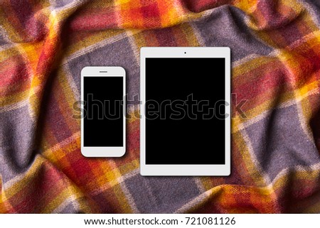 Moredn devices on warm colorful coverlet: digital tablet and smart phone with blank screens. Domestic atmosphere. Unrecognizable person spends free time at bed, uses gadgets