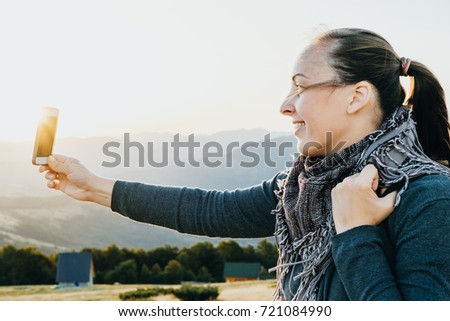 Smiling Woman traveler takes selfie on the phone mountains at dawn