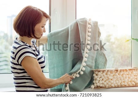 Interior designer shows samples of fabrics and accessories for curtains in the new house. Picture in the window background.