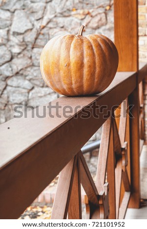 Orange autumn. A large ripe pumpkin lies on a flat wooden railing of the veranda close up
