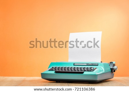 Retro old mint green typewriter with paper sheet on wooden desk front orange wall background. Vintage instagram style filtered photo