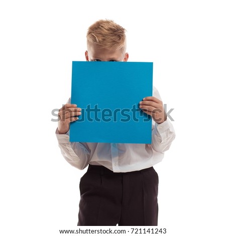Emotional blond boy in striped sport shirt holding a blue sheet of paper for notes, posing on white background