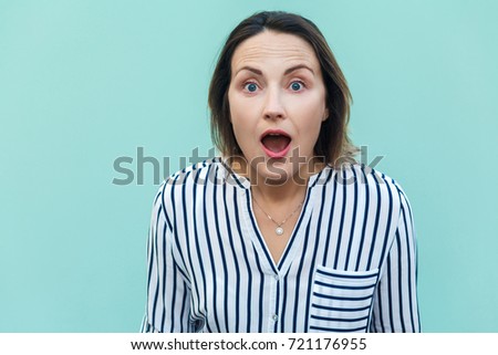 Wow! Amazed and shocked beautiful adult lady looking at camera with shocked face. Isolated on light blue background.