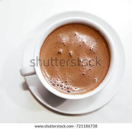 Cappuccino or hot chocolate with frothy foam, white coffee cup top view closeup isolated on white background.
