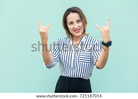 Rock n roll. Funny business lady looking at camera with rock sing. Studio shot, on light blue background.