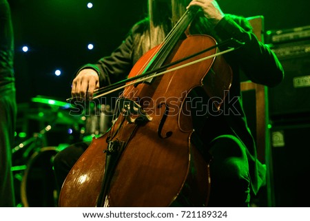 Man playing on cello on stage during concert backlight, colors intentionally altered