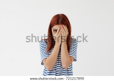 Picture of shy timid teenage girl with colored hair covering face with hands and peeping through her fingers at camera. Young woman hiding her face being frightened, scared or ashamed. Body language Royalty-Free Stock Photo #721217890