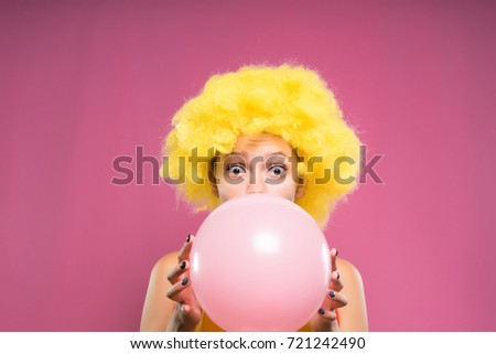 A surprised girl clown in a wig inflates a ball to her birthday. Bubble of pink chewing gum