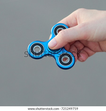 female hand holding popular fidget spinner toy on gray background, anxiety relief toy, anti stress and relaxation fidgets 