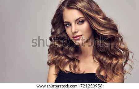 Brunette  girl with long  and   shiny curly hair .  Beautiful  model woman  with curly hairstyle. Care and beauty of hair Royalty-Free Stock Photo #721253956