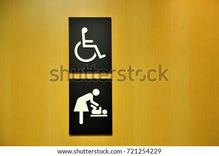 Wheelchair and women with baby sign in public washroom toilet on wooden door background.
