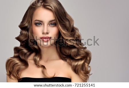 Brunette  girl with long  and   shiny curly hair .  Beautiful  model woman  with curly hairstyle   .Care and beauty of hair Royalty-Free Stock Photo #721255141