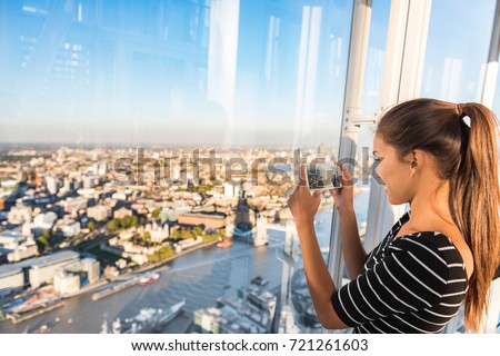 Tourist girl taking phone picture of sunset london skyline view from The Shard. Europe travel tourism.