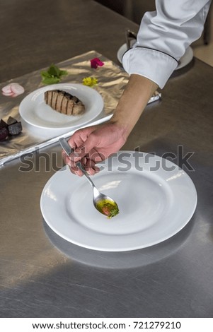 Chef manipulating different utensils for the assembly of a strong dish that has meat, vegetables and flowers for the decoration