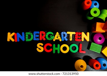 Colorul plastic letters spelling text KINDERGARTEN SCHOOL with colorful wooden shape on black background