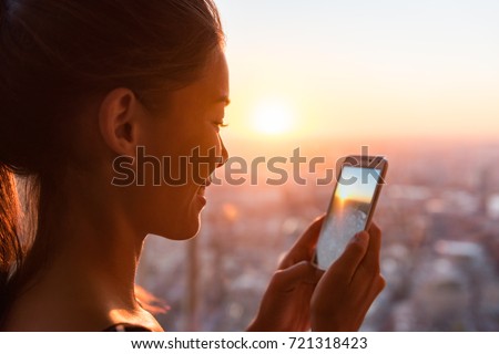 Woman tourist looking at phone pictures of sunset view of Europe travel destination. Asian girl using cellphone camera app in London Shard Tower, UK. Mobile photography taking photos.