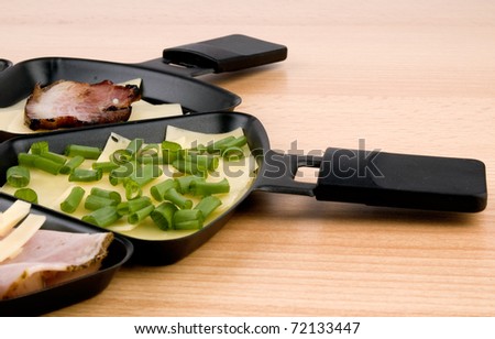 Closeup picture of raclette pan with cheese, becon and spring onion