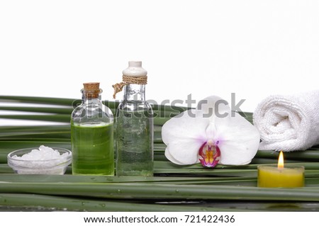 Spa setting with white orchid ,salt in bowl, oil ,candle, towel on palm leaf
