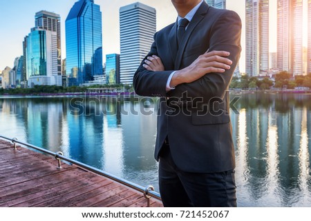 Confident Business Concept, Businessman pose crossed arms on wooden terrace at lake and city town  background