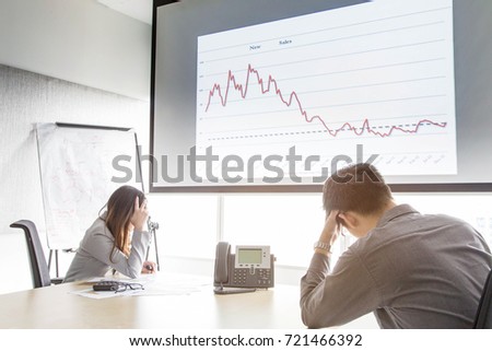 Serious and fail business man and woman in meeting room with 
negative graph on screen. They are waiting consultant form conference telephone Royalty-Free Stock Photo #721466392