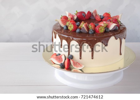 Cake in chocolate, decorated with slices strawberries, blueberries and figs on a white wooden table in the morning sun. Picture for a menu or a confectionery catalog with copy space.
