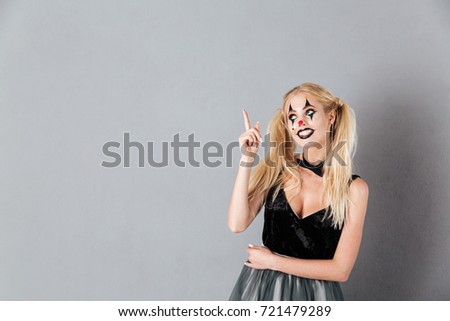 Smiling blonde woman in halloween make-up pointing and looking up over gray background