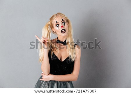 Pensive blonde woman in halloween make up having idea and looking away over gray background