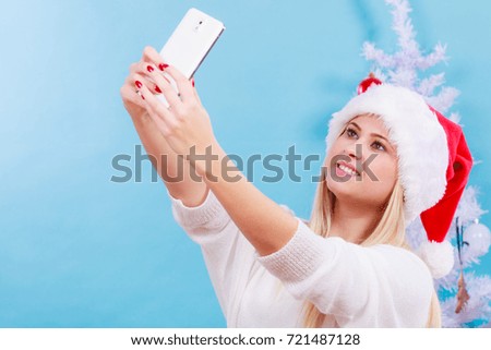 Modern holiday concept. Blonde woman in Santa hat taking Christmas picture of herself, selfie with smartphone.
