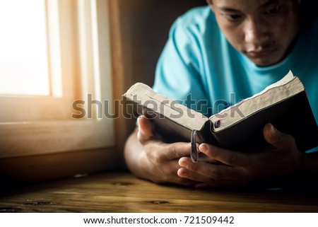 Male reading Bible on wooden desk at home