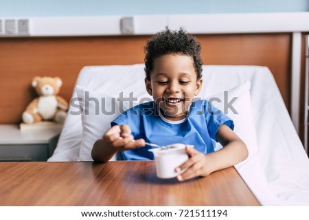 portrait of little african american boy eating yogurt while resting in hospital bed Royalty-Free Stock Photo #721511194