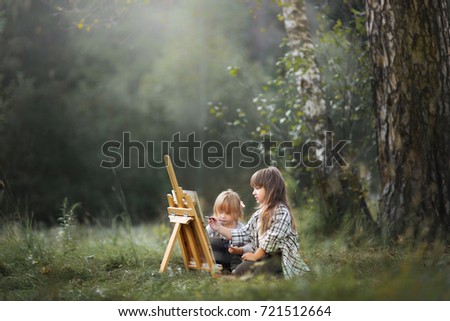 Little sisters painting at easel in autumn park 