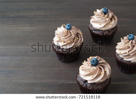 Chocolate cupcakes with whipped chocolate cream, decorated fresh blueberry, gold confectionery sprinkling on dark wooden table. Picture for a menu or a confectionery catalog.