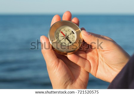 Hands holds a compass indicating the direction of the background of the sea