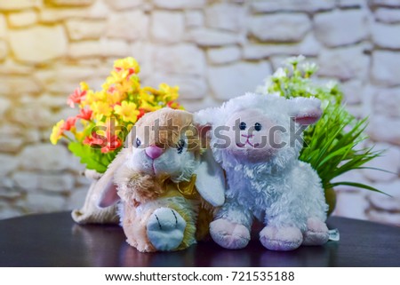 Rabbit and sheep dolls are on the table with flowers.