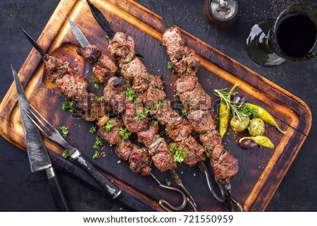 Traditional Russian shashlik on a barbecue skewer and red wine as top view on an old burnt cutting board 