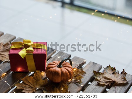 pumpkin and gifts with maple leaves and Fairy Lights around on a wooden table near a window in rainy day. Autumn season image