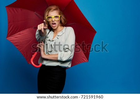 young woman with glasses with an amazed face holds a red umbrella on a blue background                               