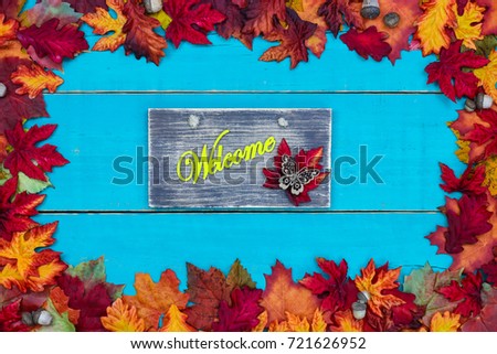 Welcome sign with butterfly and colorful fall leaves border with acorns hanging on antique rustic teal blue wood background; autumn, Thanksgiving, Halloween, seasonal nature sign 