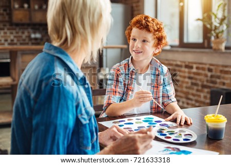 What do you think about my picture. Selective focus on an excited boy smiling to his grandmother while both having a pleasant conversation and painting at a table.