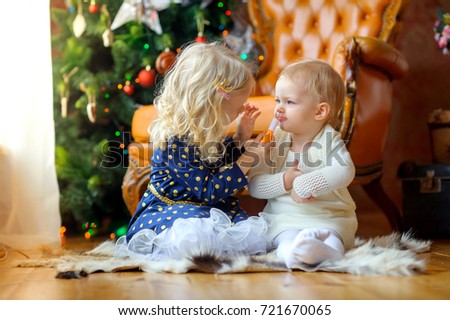 two little girls play with lipstick sitting on the floor, in the background a festive Christmas tree